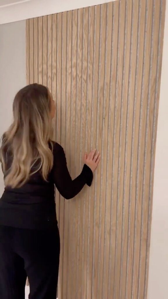 A woman touching vertical light wood slat acoustic panels installed on a wall.