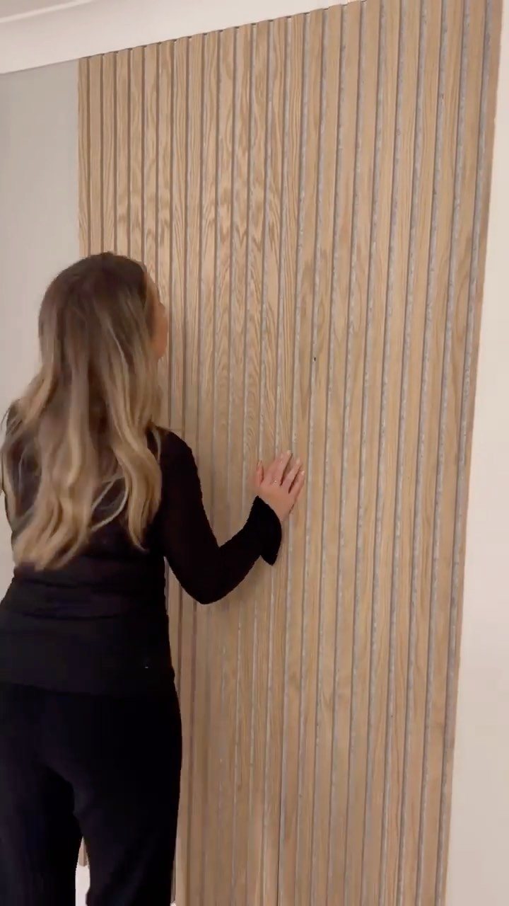 A woman touching vertical light wood slat acoustic panels installed on a wall.