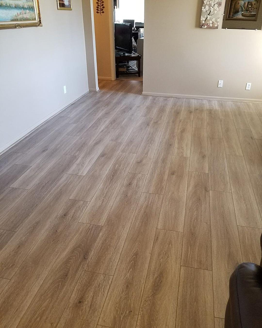 Light brown wood-textured laminate flooring planks installed in a bright room with white walls.