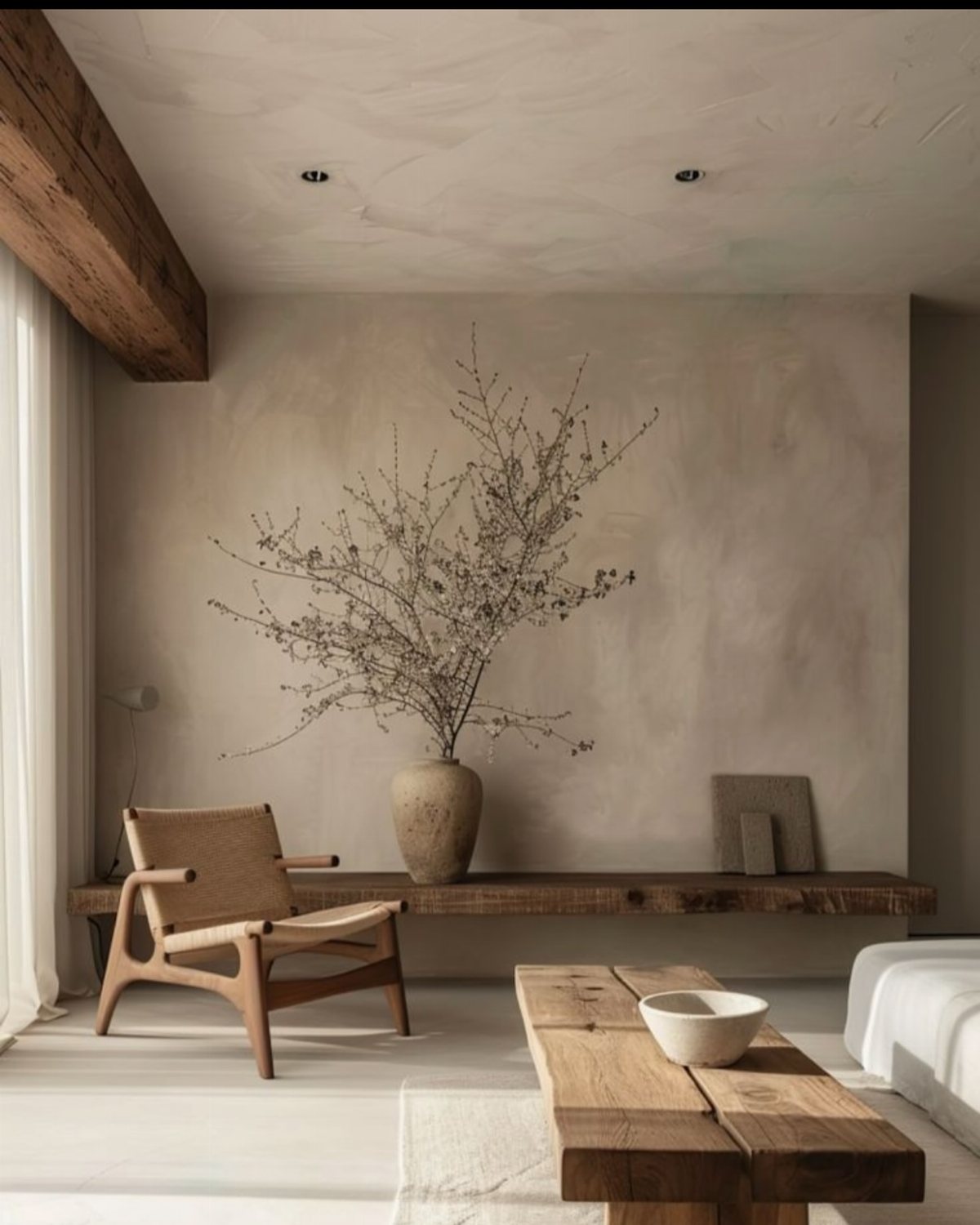 A textured beige limewash wall in a minimalist room with wooden furniture and dried branches.
