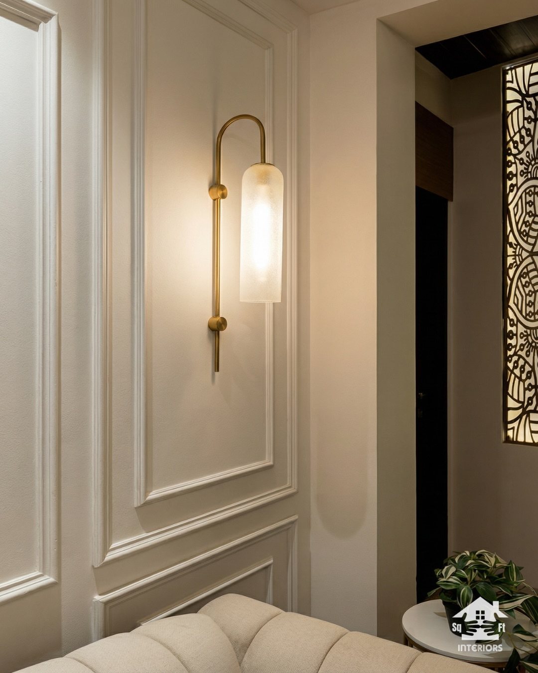 White decorative wall molding with rectangular panels and a gold modern wall sconce.