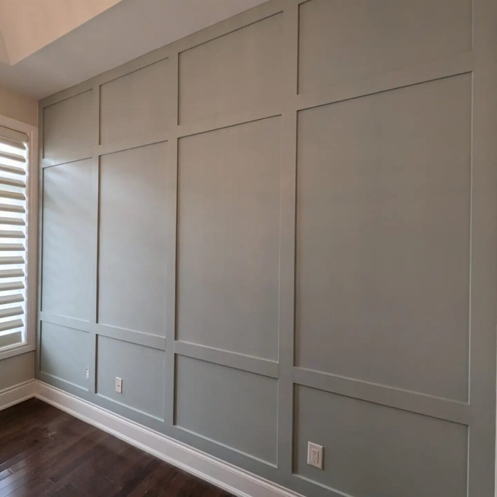 Light grey wall with large rectangular picture frame molding and dark wood floors.