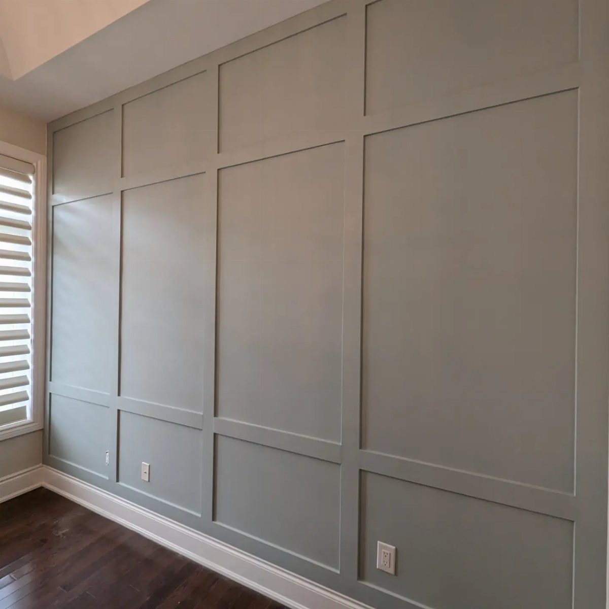 Light grey wall with large rectangular picture frame molding and dark wood floors.