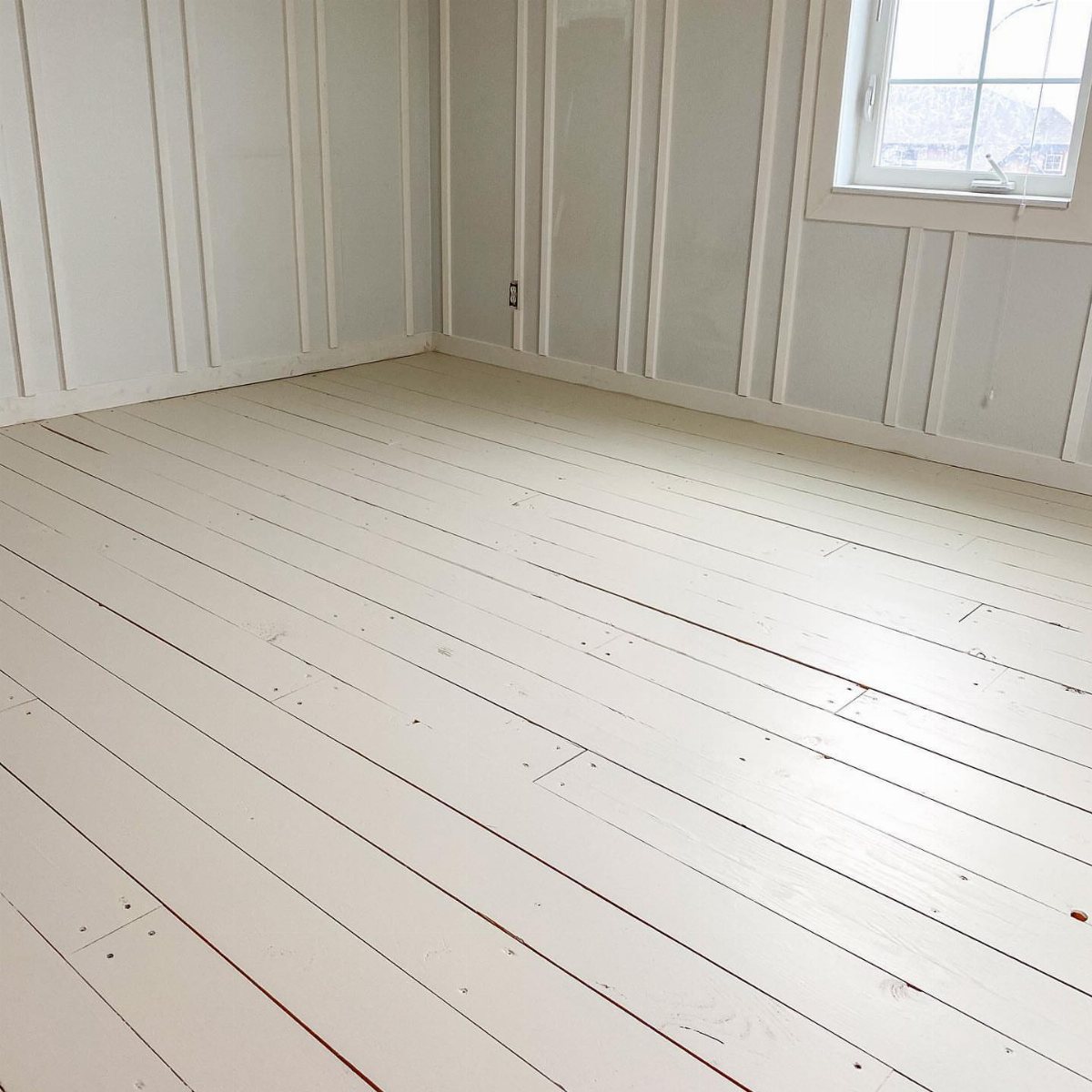 White painted wooden floorboards in a room with matching white paneled walls.