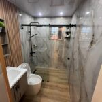 Modern bathroom with marble patterned wall panels, glass shower, and wood-look flooring.