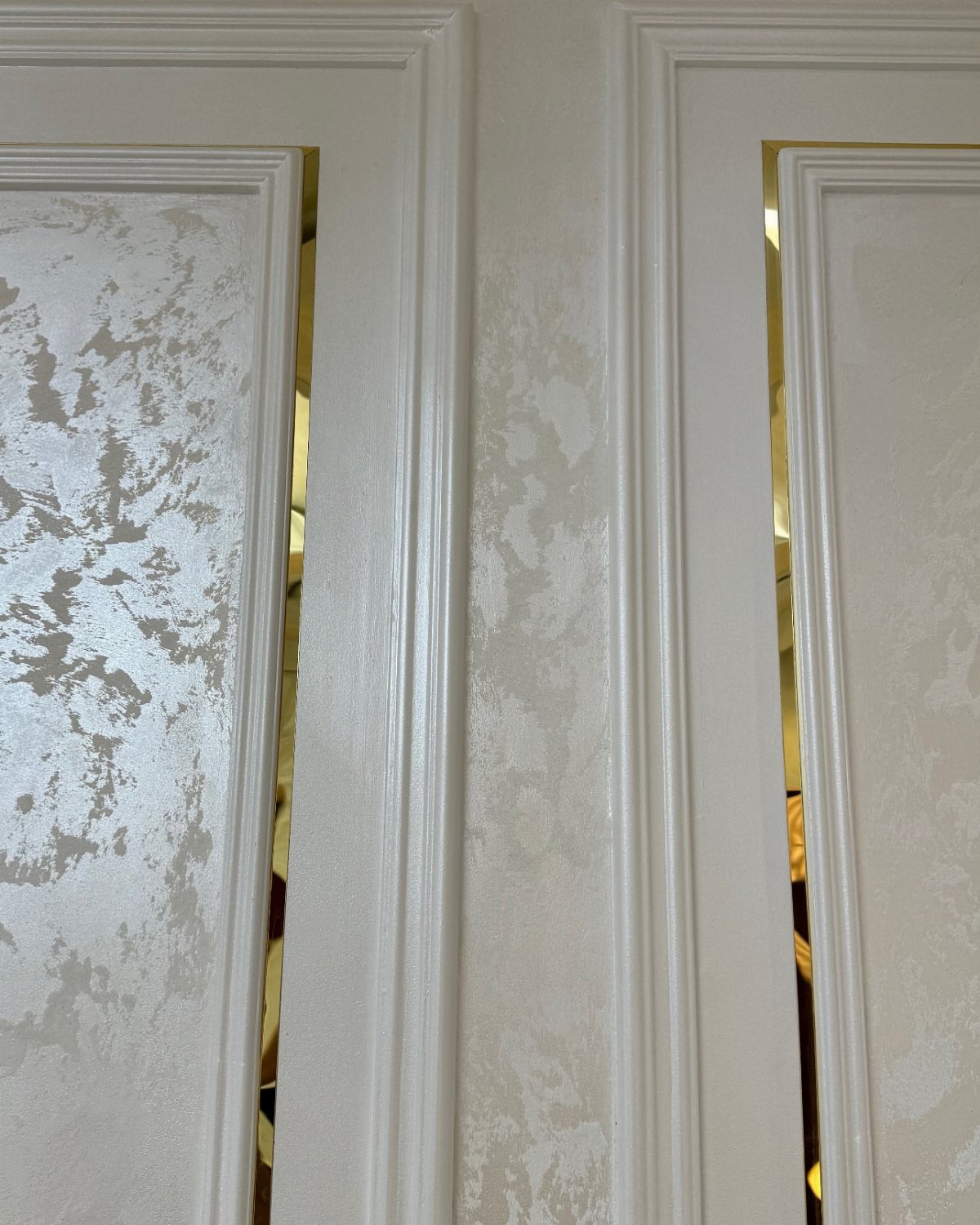 White decorative wall moulding framing textured panels with gold accents in a room.